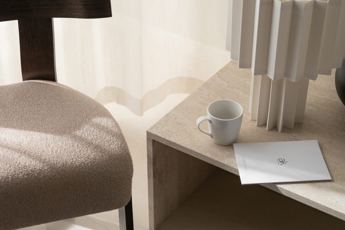 Moderne sidebord med skulpturel hvid lampe, kop og notesbog ved stol