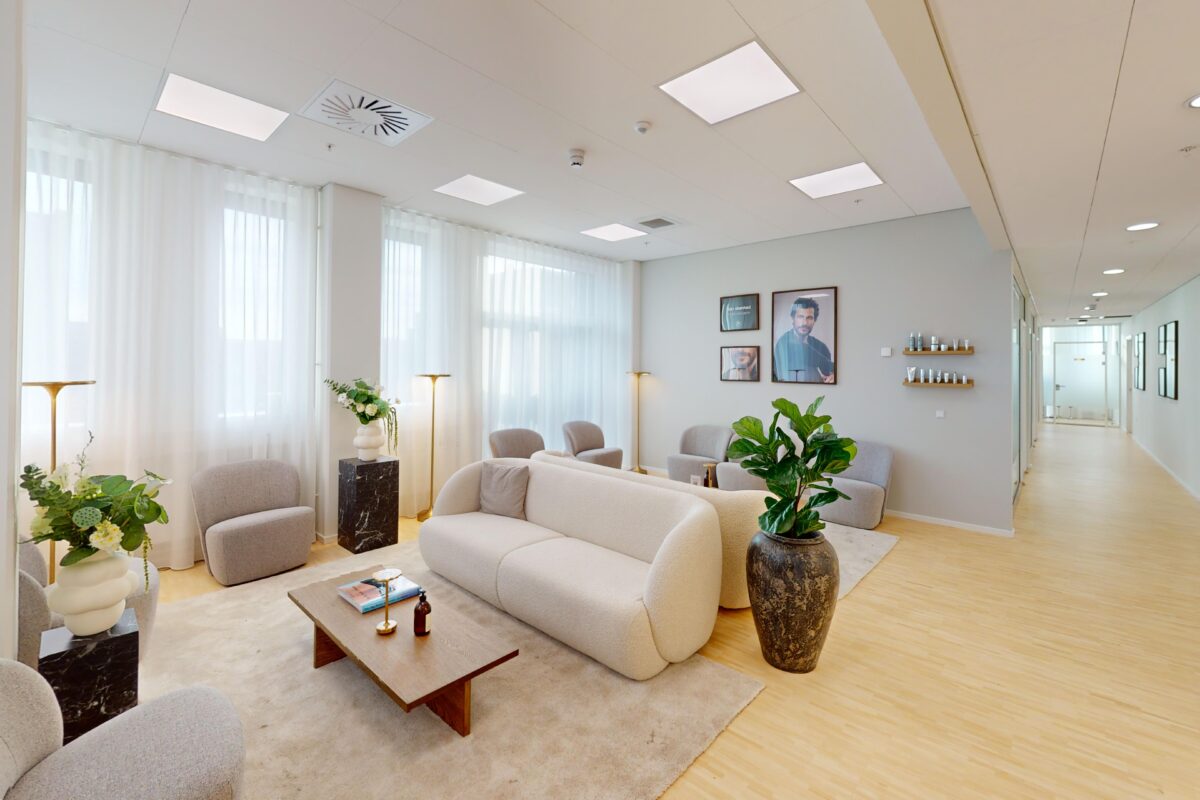 Moderne venteværelse med beige sofa, lænestole, planter og store vinduer med hvide gardiner