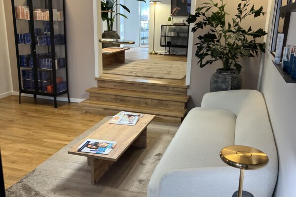 Moderne venteområde i klinik med beige sofa, træbord, planter og produkthylde